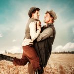 two men holding each other in a wheat field