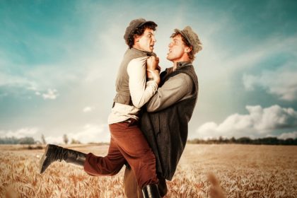 two men holding each other in a wheat field